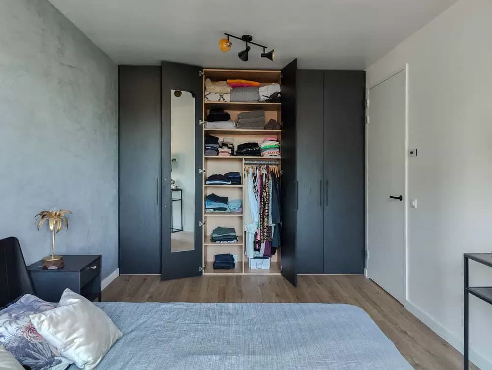 Ingebouwde zwarte kledingkast met open deuren en georganiseerd interieur in een slaapkamer in Blaricum.